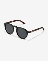 Lentes de sol Hawkers unisex, modelo Warwick, con montura redonda negra y patillas Carey.