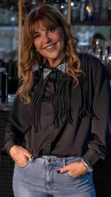 Camisa negra de manga larga con cuello camisero adornado con piedras brillantes y flecos largos en el frente.