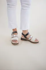 Sandalias de cuero color blanco y plateado, con tiras anchas y ajuste con hebilla. Suela track color caramelo.