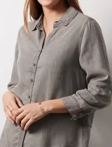 Camisa gris de tencel con cuello con solapa, escote en V y abertura central con botones. Largo de manga regulable con presilla y botón. Ruedo en espalda con tajo.
