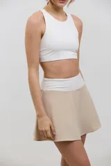 Pollera deportiva de corte acampanado color beige, con calza corta integrada de color blanco. Presenta cintura ancha de tiro alto y bolsillo invertido en la calza para guardar pelotas.