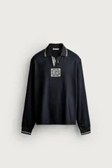 Polo relaxed fit de manga larga confeccionado en tejido técnico negro con textura acanalada, cuello solapa con ribete blanco y abertura frontal. Incluye parche conmemorativo England 66 Fifa World Cup en el pecho y puños con ribetes a contraste.