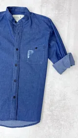 Camisa de jean azul marino, con cuello mao, manga larga con puños abotonados, cierre frontal con botones y bolsillo en el pecho con detalle de rotura.