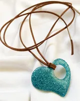 Gargantilla con tiento de cuero marrón y dije de corazón turquesa con glitter. El dije tiene un agujero en la parte superior por donde pasa el tiento.