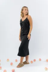 Vestido midi celeste de tejido tipo seda fría, con breteles finos regulables, botones de madera decorativos en el frente, pliegues decorativos en la cintura y cierre invisible en el costado.