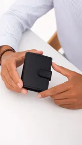 Tarjetero compacto de símil cuero negro con cierre de presilla metálica. Posee múltiples ranuras para tarjetas, visor transparente para documentos, compartimento para billetes y bolsillo exterior con cierre para monedas.