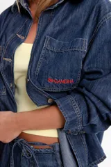 Camisa de jean azul oscuro, de corte oversize, con mangas largas y puños abotonados. Presenta bordados rojos en el pecho y un parche denim con el logo "BG" en la espalda.