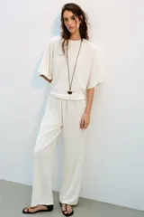 Top blanco de tejido rústico, con cuello redondo y mangas cortas amplias. Bajo recto.