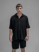 Camisa de corte oversize color negro, confeccionada en lino, con cuello tipo cubano, cierre frontal de botones y mangas cortas.