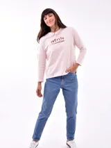 Remera de manga larga color blanco, con cuello redondo y estampa frontal en tono rosado que incluye un diseño de marco con moño y la frase "live simply love sincerely".