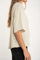 Blusa cruda con estampado de lunares negros, de manga corta y cuello redondo.