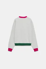 Sudadera gris melange de la colección especial Fruit of the Loom x Zara, con cuello redondo fucsia con abertura y botones, mangas largas con puños fucsias, y ribete inferior verde oscuro. Cuenta con logo bordado multicolor en el pecho.