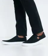 Championes tipo slip on marca Viko, de color negro con suela de goma blanca. Presenta un diseño minimalista sin cordones con paneles elásticos laterales y un pequeño detalle de etiqueta en color marrón.