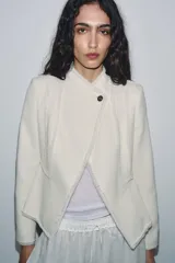 Blazer de cuello alto confeccionada en mezcla de algodón con textura tipo tweed. Presenta un diseño con acabados desflecados, cierre frontal con un solo botón y bajo con detalle peplum.