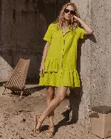 Vestido camisero corto de lino verde lima, con mangas cortas, cierre frontal de botones, volado en el ruedo y un volado asimétrico aplicado en un lateral.
