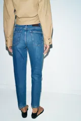 Jeans de tiro alto con corte mom fit, diseño de cinco bolsillos y raya planchada frontal. Presenta cierre frontal con cremallera y botón.
