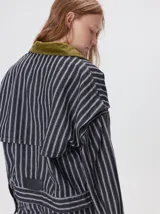 Campera de denim a rayas verticales con cuello de pana en color bordó. Presenta cierre frontal, mangas desmontables con cierre en los hombros, canesú en el pecho y bolsillos de parche cuadrados.