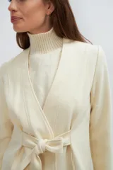 Chaqueta corta color beige, entallada, con escote en V, manga larga y bolsillos escondidos. Cierre frontal con lazo fijo. Confeccionada en lana fina sin teñir. Diseño exclusivo de Don Baez.