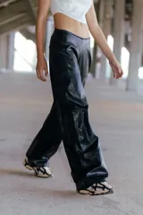 Pantalón cargo de ecocuero negro, de corte holgado y tiro medio-alto. Presenta bolsillos laterales tipo cargo y costuras visibles a lo largo de las piernas.