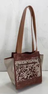 Cartera de cuero de la marca Carolina De Cunto, modelo Nia de la línea Ottenta Basic. Presenta diseño combinado en tonos marrón y tostado con detalles en pelo natural con estampado animal print, bolsillos con cierre exterior e interior, porta llaves y doble asa de hombro.