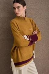 Buzo tejido de silueta amplia con cuello alto, mangas largas y puños en contraste. Presenta un diseño con franjas horizontales en el ruedo y detalles de tejido trenzado en las mangas.