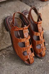 Sandalias de cuero color suela con textura efecto cocodrilo, diseño de tiras cruzadas tipo gladiadora, taco bajo y tira ajustable en el tobillo con hebilla redonda.