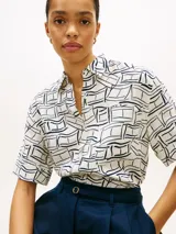 Camisa de manga corta Tommy Hilfiger de corte amplio y hombros ligeramente caídos, confeccionada en puro lino blanco con estampado geométrico de líneas azules. Cuenta con cuello inglés, cierre frontal de botones, bolsillo de parche en el pecho y logo bordado.