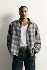Camisa de algodón con corte boxy fit, diseño a cuadros en tonos grises y blancos, cuello clásico y manga larga con puños abotonados.