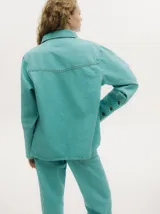 Campera de denim con efecto gastado, cuello camisero, cierre frontal con botones metálicos y corte holgado. Presenta canesú con costuras decorativas en el frente y la espalda, y botones en los puños.