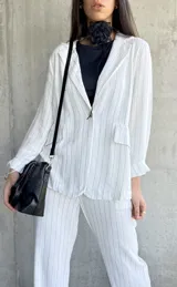 Blazer blanco con finas rayas verticales negras, solapas clásicas, cierre con un botón y bolsillos frontales.