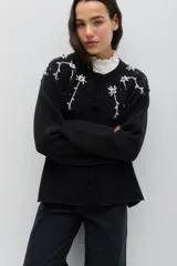 Saco de punto color rosa, con cuello redondo, cierre frontal con botones forrados en crochet y mangas largas. Presenta un delicado bordado floral artesanal que cae desde los hombros y detalles de calados en los puños y el ruedo.