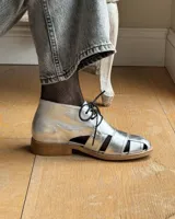 Zapato acordonado de cuero vacuno color marrón con aberturas laterales y cordones negros.