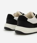 Championes urbanos de hombre, modelo street, color negro y blanco. Presenta capellada de material sintético (PU) con recortes, puntera redonda, cordones negros y paneles de malla blanca para ventilación. Posee una suela gruesa (bold) de color blanco y negro.