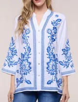 Blusa blanca con bordados florales en azul, de manga tres cuartos y cuello mao con escote en V.