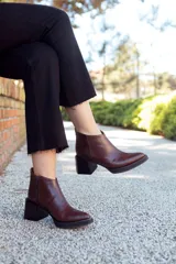 Botines de cuero color marrón oscuro con puntera fina y caña baja. El talón es de cuero con textura de reptil y el taco es geométrico.