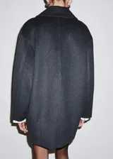 Abrigo de paño negro con cuello clásico, cierre frontal de botones y bolsillos laterales. Presenta un corte recto y holgado con mangas largas.