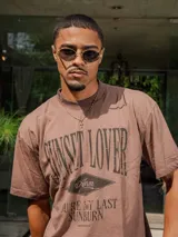 Remera de jersey con efecto teñido, color marrón, de corte holgado y cuello redondo. Presenta un estampado frontal con texto en tonos más oscuros.