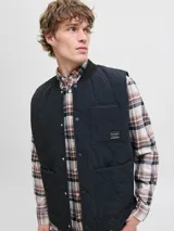 Chaleco acolchado negro con diseño de costuras onduladas, cuello estilo baseball y cierre frontal con botones a presión. Cuenta con dos bolsillos frontales de parche y un bolsillo pequeño en el pecho con etiqueta de marca.