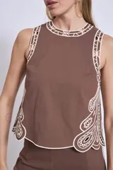Blusa negra sin mangas, de corte recto y escote redondo, con detalles de bordados contrastantes en color blanco en los bordes y costados.