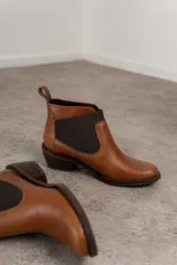 Botín negro de cuero con elásticos laterales, taco bajo y tirador trasero.