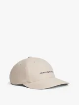 Gorra de seis paneles color beige claro, confeccionada en algodón, con visera curva rígida y ojales bordados. Presenta el logo de Tommy Hilfiger bordado en el panel frontal.
