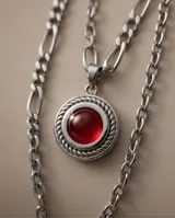 Collar de acero con diseño de doble cadena y dije circular con piedra central roja rodeada por un detalle trenzado.