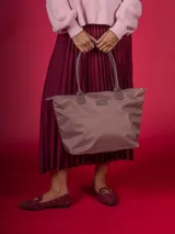 Bolso tipo shopper de nylon color rosa pálido/malva, con asas y detalles en cuero sintético marrón grisáceo. Presenta un parche con el logo de la marca en el frente.