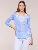 Blusa celeste con estampado floral devoré, de manga tres cuartos, escote redondo amplio y detalle de pechera de encaje blanco en contraste.