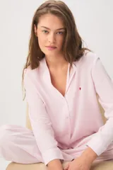 Pijama rosado de 100% viscosa con diseño a rayas sutiles, compuesto por una camisa de manga larga con cuello solapa y botones delanteros, y un pantalón largo de corte holgado con cintura elástica y cordón ajustable. Presenta un pequeño detalle bordado de corazón rojo en el pecho de la camisa.
