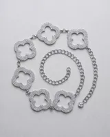 Cinto de cadena metálica plateada con eslabones y dijes en forma de trébol de cuatro hojas decorados con strass brillante.