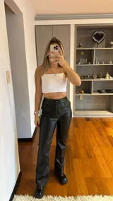 Pantalón negro de cuerina con tiro alto y corte acampanado, destacando por sus costuras blancas a la vista.