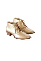 Botín de caña baja con cordones, confeccionado en cuero vacuno metalizado color dorado. Presenta puntera redondeada y tacón bloque texturizado en tono madera.