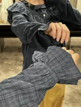 Camisa blanca de textura rugosa con volados en el pecho y hombros, cuello redondo con lazos de ajuste, cierre frontal con botones y mangas largas con puños con volados.