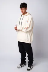 Buzo canguro amarillo ocre oversize de algodón rústico con capucha, cordones negros con letras blancas, bolsillo frontal y puños y cintura acanalados. Presenta estampados en el frente y las mangas.